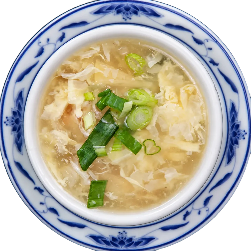 Egg drop soup with green onions in a blue and white bowl